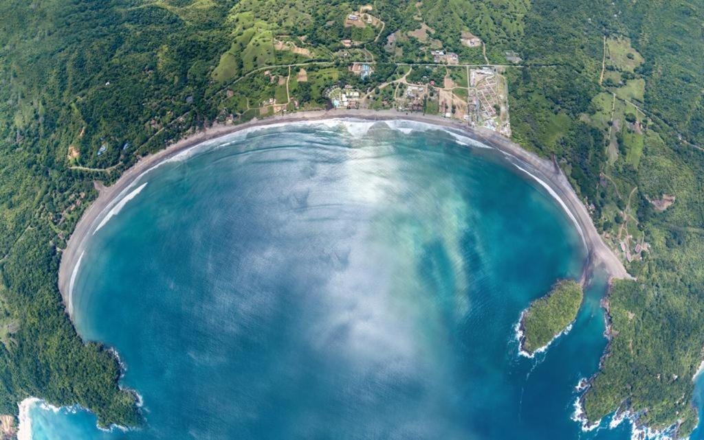 Aerial view looking straight down on the Playa Venao bay, its beach curving between forested hills